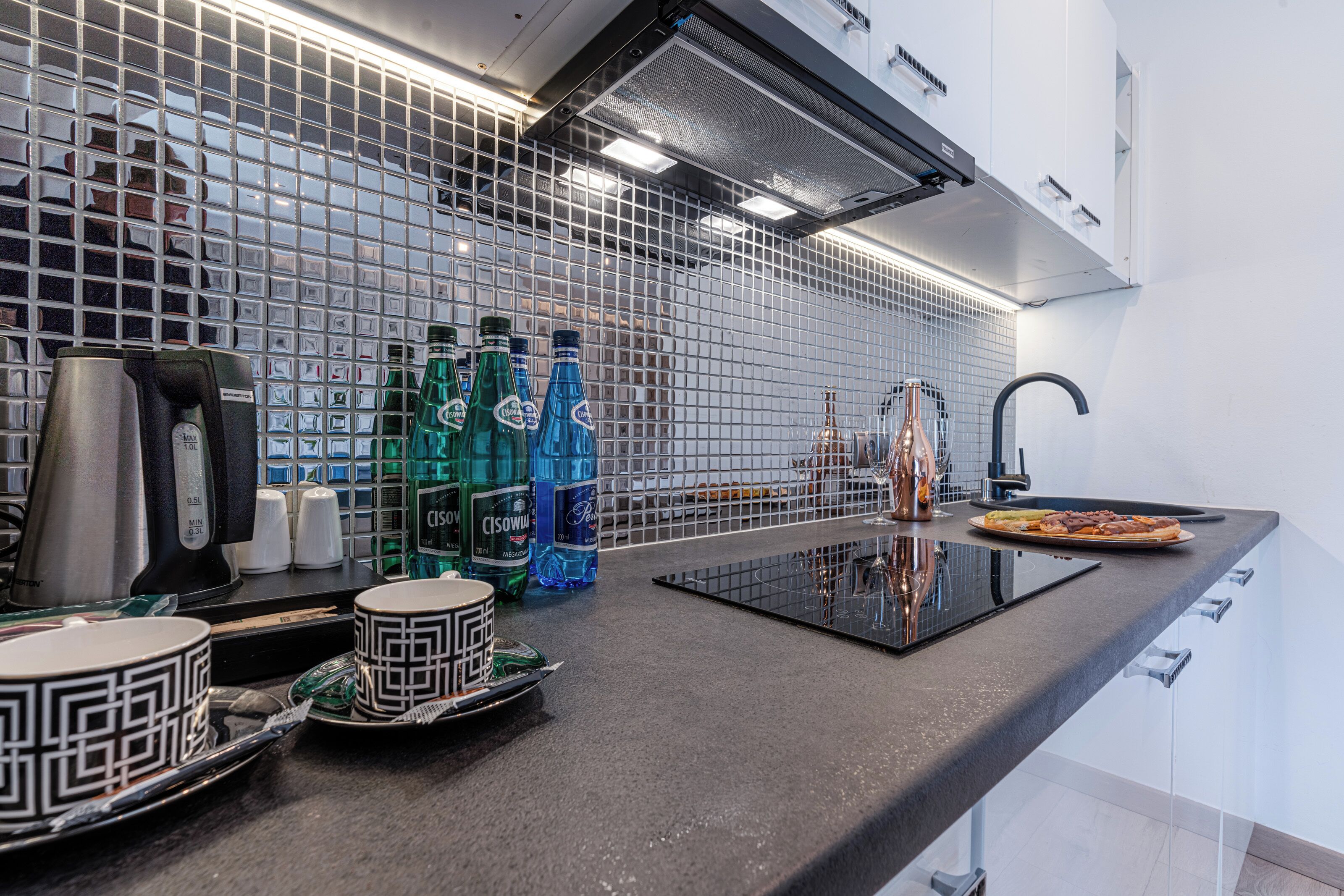 A modern kitchen with a black countertop, a built-in stove, and a backsplash of small tiles.