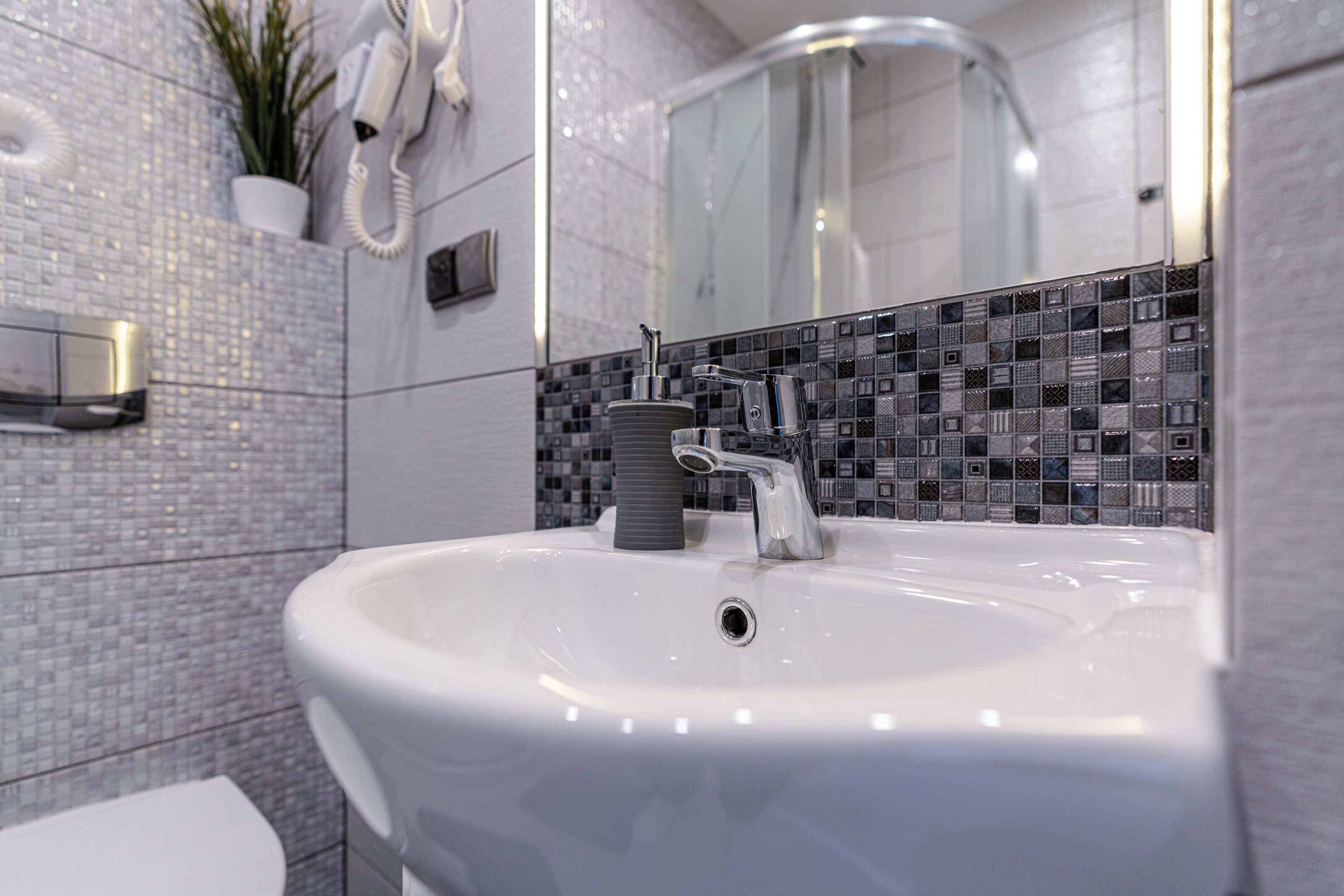 A modern bathroom with a white sink, a handheld showerhead, and a mirror above the sink.