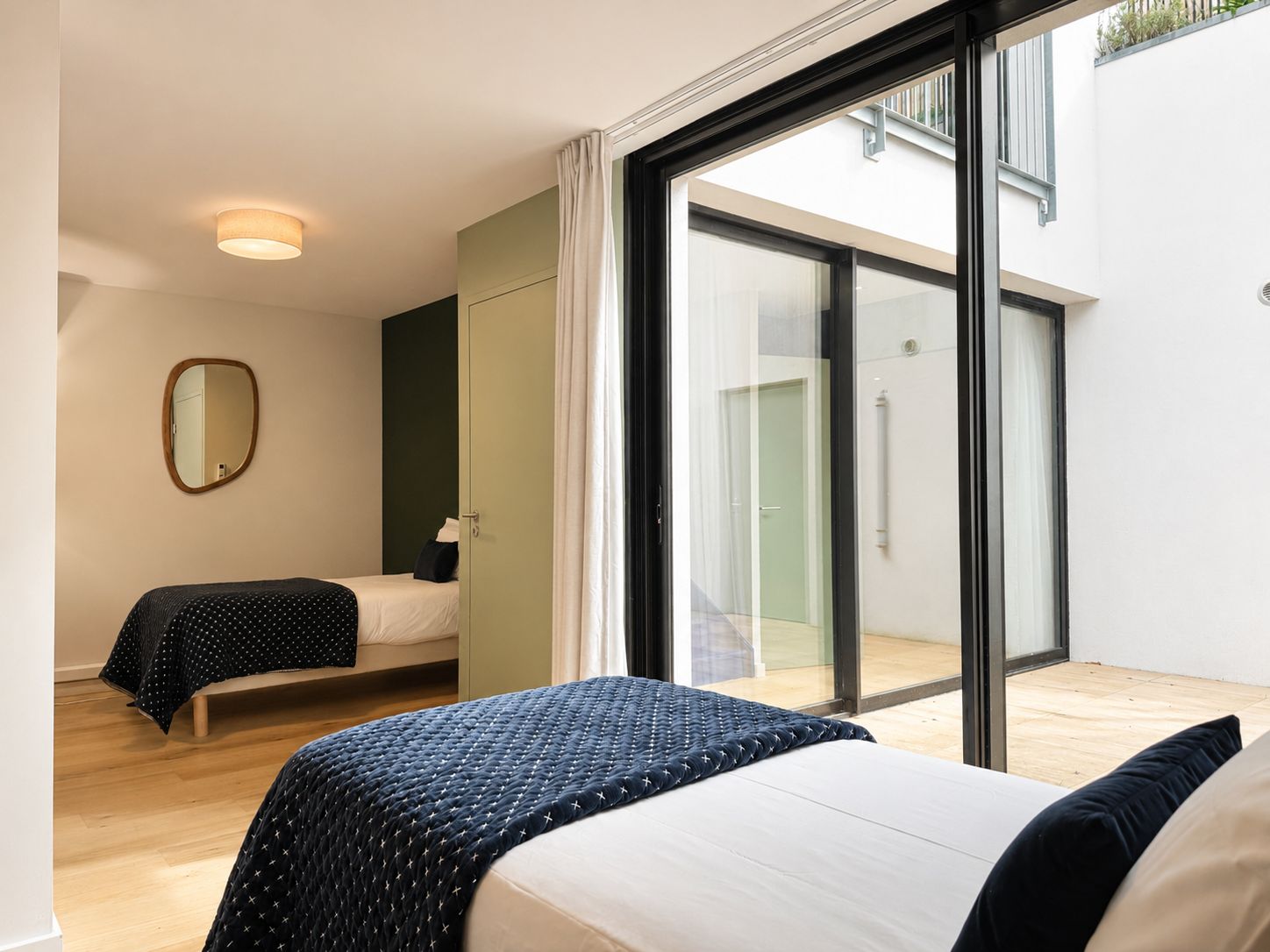 Een moderne slaapkamer met twee bedden, een grote schuifdeur naar een balkon en een spiegel aan de muur.