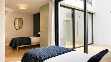 Een moderne slaapkamer met twee bedden, een grote schuifdeur naar een balkon en een spiegel aan de muur.