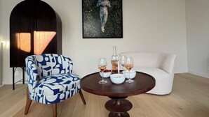 Ein modernes Wohnzimmer mit einem runden Holztisch, einem blau-weißen Ohrensessel, einem weißen Sofa und einem gerahmten Kunstwerk mit einem Astronauten an der Wand.