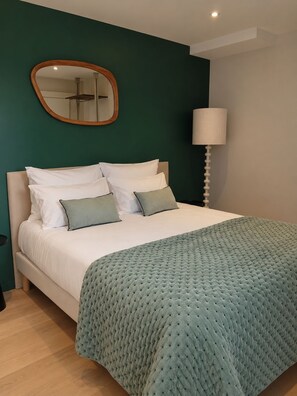 Une chambre à coucher avec un lit, des oreillers, une lampe de chevet et un miroir au mur.