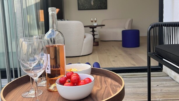 Ein Holztablett mit einer Flasche, Gläsern und einer Schale Tomaten auf einem Balkon.