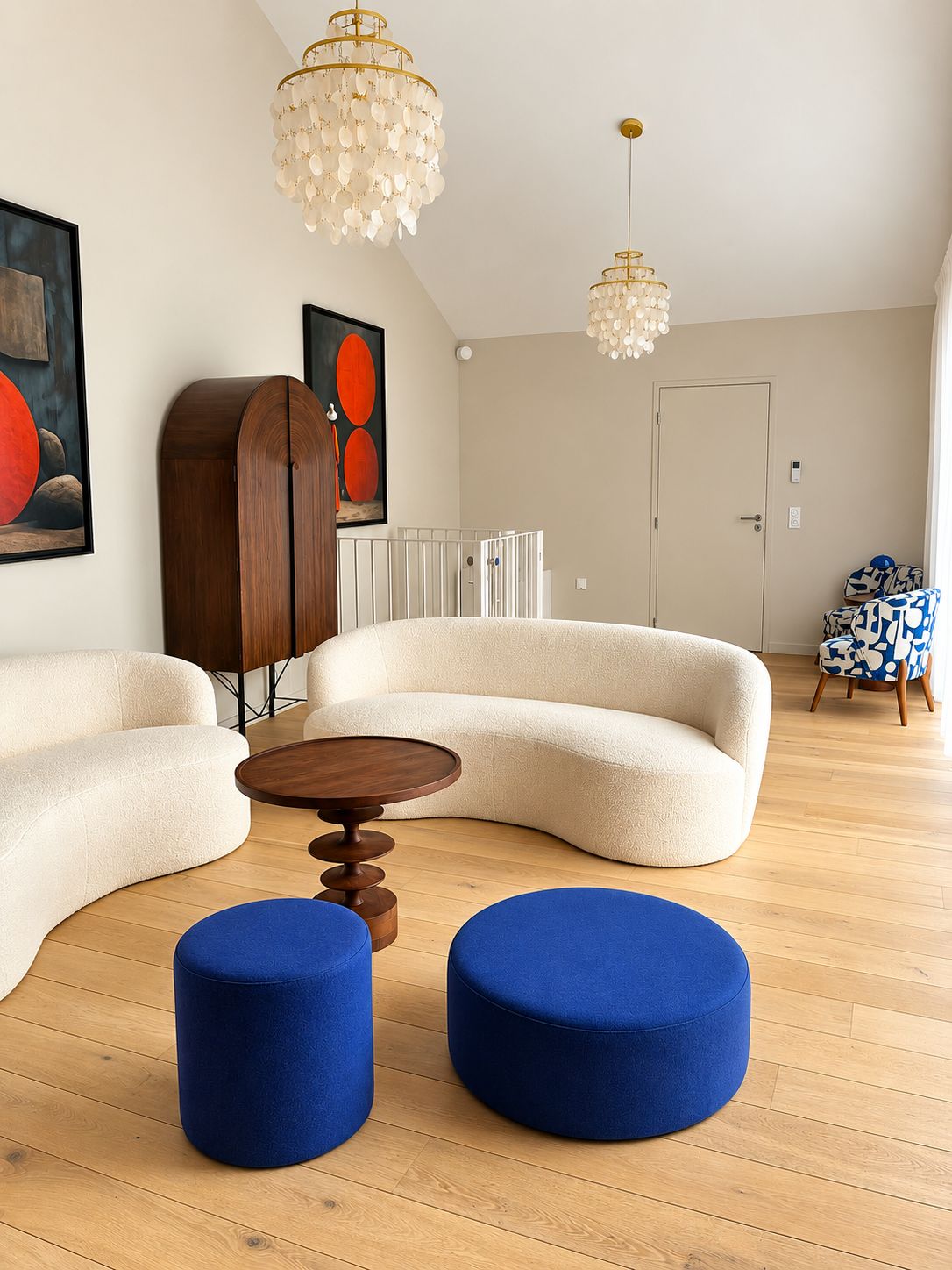 Een moderne woonkamer met een gebogen bank, twee blauwe voetenbankjes, een houten salontafel en twee kroonluchters.