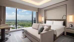 Una habitación de hotel moderna con una cama grande, un sofá, una mesita pequeña y una mesita de noche.