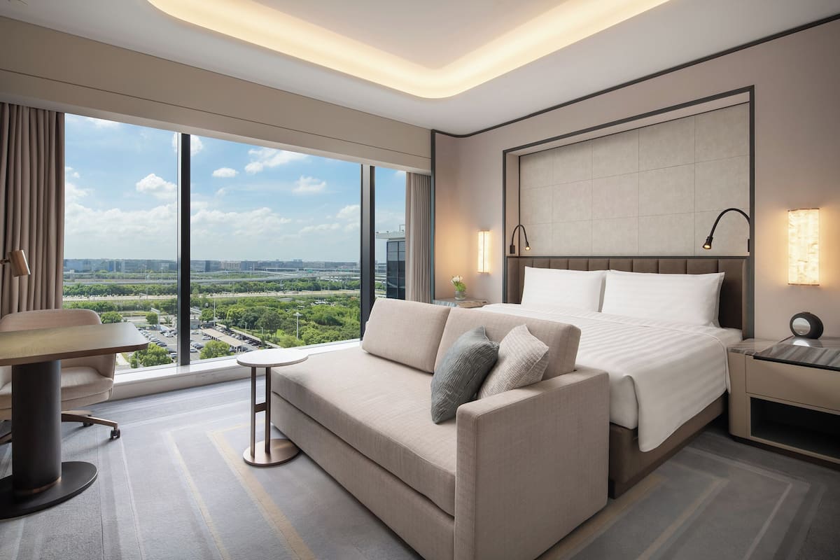 A modern hotel room with a large bed, a sofa, a small table, and a nightstand.