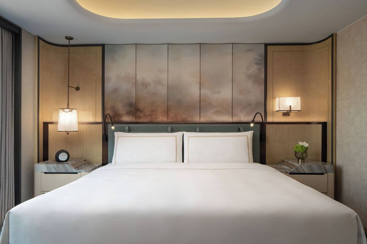 A modern hotel room with a large bed, two bedside tables, and a unique ceiling design.
