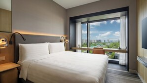 Ein modernes Hotelzimmer mit einem großen Bett, einem Schreibtisch und einem Fenster mit Blick auf die Stadt.