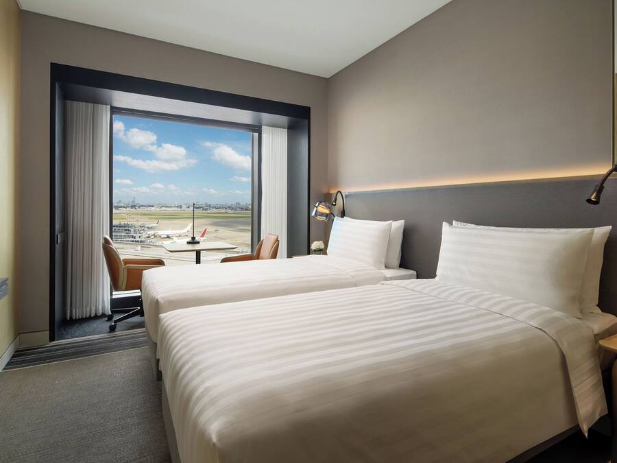 A hotel room with two beds, a desk, and a view of an airport.