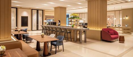 A modern hotel lobby with a central bar area, seating arrangements, and a reception desk.