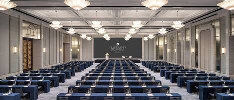 A conference room with rows of tables, a stage at the front, and chandeliers.