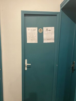 Une porte de couleur turquoise avec deux panneaux : l’un en français et l’autre en anglais, indiquant qu’il faut laisser les toilettes propres.