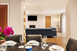 A modern living room with a fireplace, a black sofa, and a dining area with a marble table set for two.