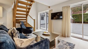 A modern living room with a wooden staircase, a sofa, a table, and a TV mounted on the wall.