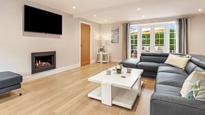 A modern living room with a fireplace, a flat-screen TV, a grey sofa, and a dining table.