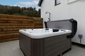 A hot tub with a wooden deck and a white wall in the background.
