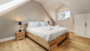 A bedroom with a sloped ceiling, a large bed, wooden nightstands, and a window with blinds.