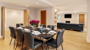A modern dining area with a round table set for six, surrounded by black chairs. A vase with pink flowers is on the table.