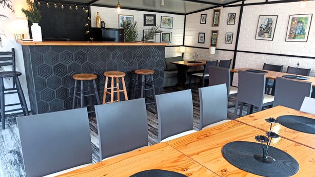 Un restaurant moderne avec une longue table en bois, des chaises grises et un coin bar doté de tabourets.