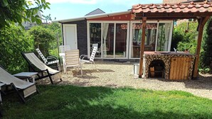 Une terrasse avec des meubles d’extérieur, un barbecue en pierre et une porte vitrée donnant sur un espace abrité.