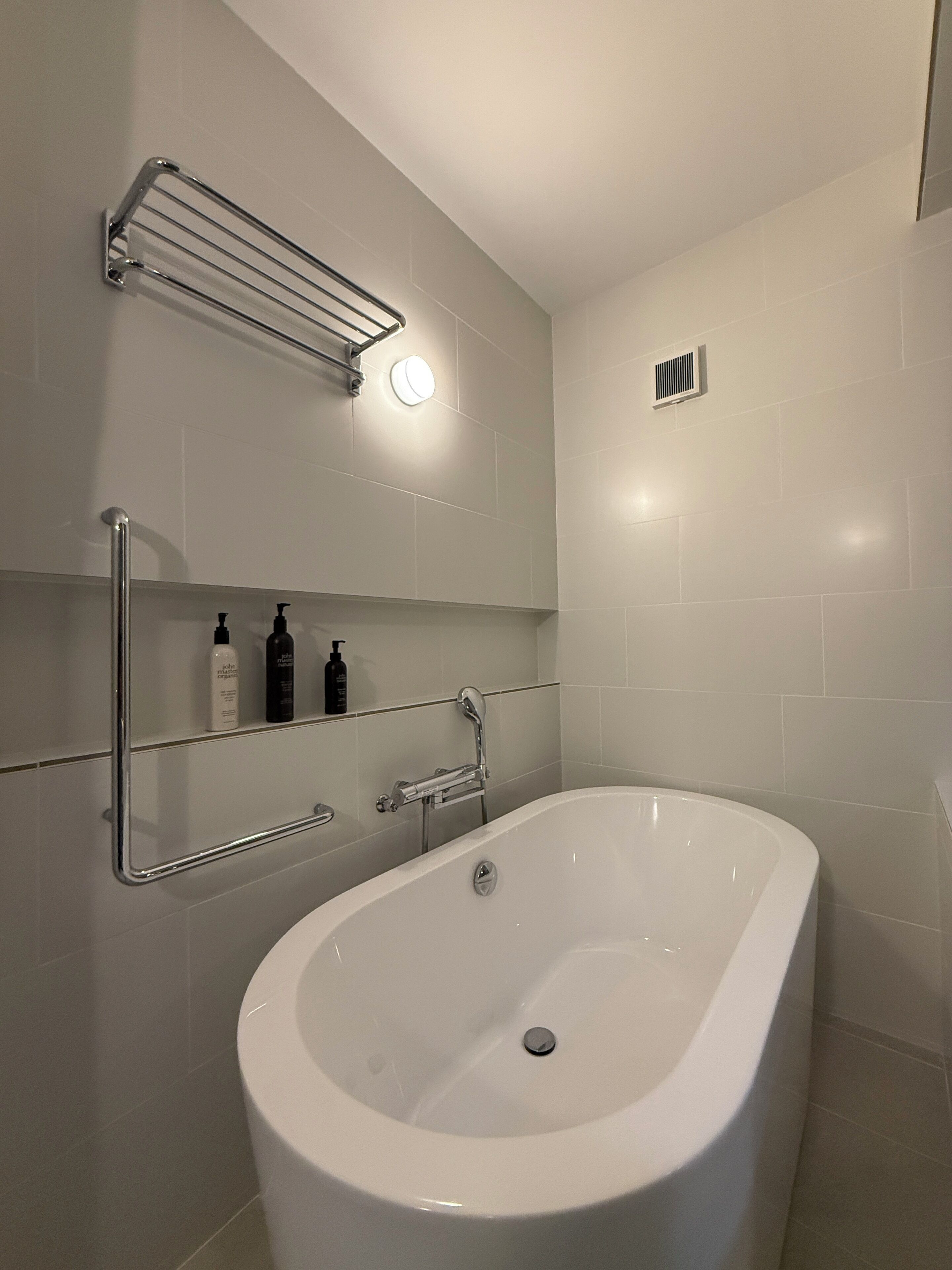 Ein modernes Badezimmer mit einer freistehenden Badewanne, einem Handtuchhalter und einem Ablagefach für Pflegeprodukte.