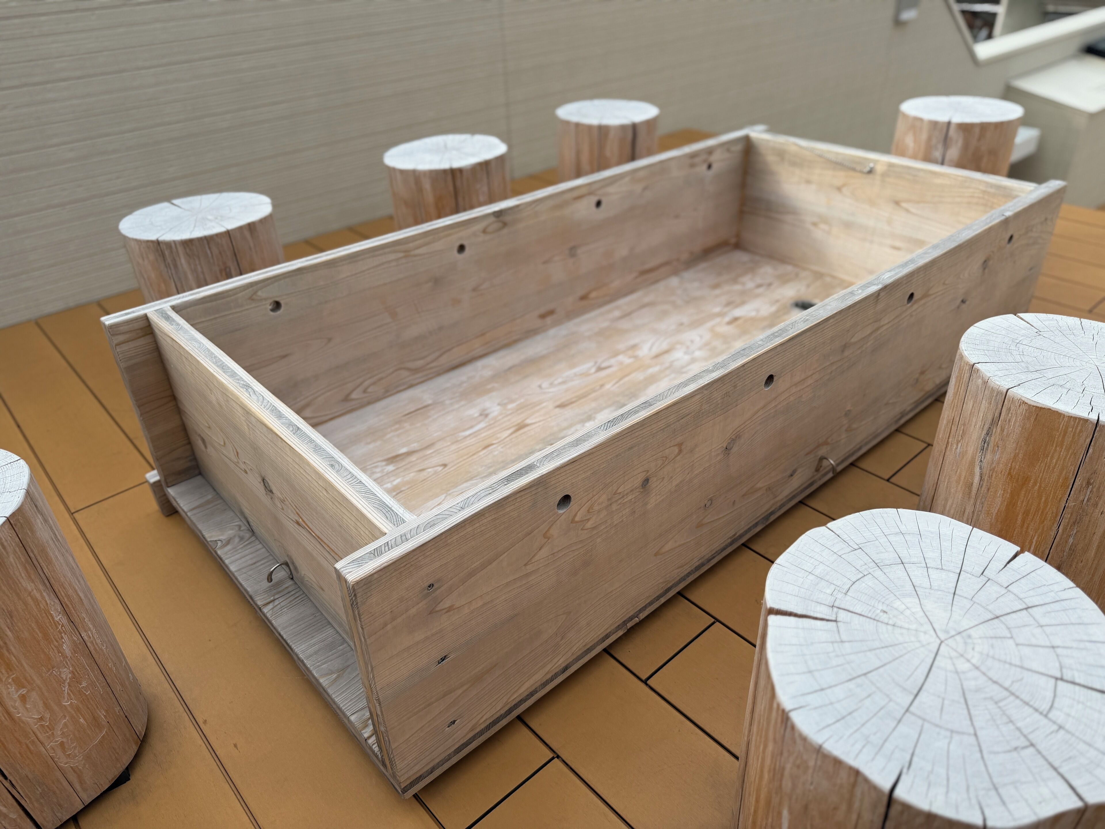 A wooden bench with a rectangular seat and backrest, surrounded by round wooden stools with white-painted tops.