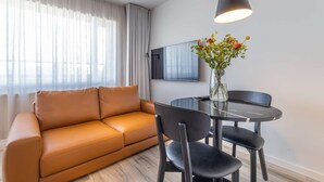 A modern living room with a sofa, a dining table with chairs, a vase with flowers, and a mounted TV. - Hlemmur Suites - Large Deluxe Studio (Reykjavík)