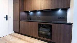 A modern kitchen with wooden cabinets, a black countertop, a sink, and an oven. - Hlemmur Suites - Large Deluxe Studio (Reykjavík)