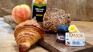 A wooden table with a croissant, a peach, a loaf of bread, a jar of jam, a carton of juice, and a bottle of cream. - Superior one bedroom apartment (Reykjavík)