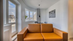 A modern living room with a sofa, a dining table with chairs, and a pendant light. - Deluxe Ocean view one bedroom apartment with balcony (Reykjavík)