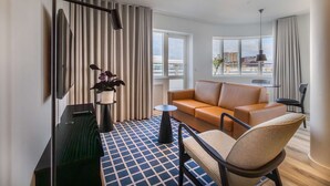 A modern hotel room with a sofa, a chair, a small table, a floor lamp, and a potted plant. - Deluxe Ocean view one bedroom apartment with balcony (Reykjavík)