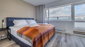 Una habitación de hotel con cama, mesita de noche, ventana con vista al mar y radiador.