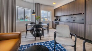 A modern kitchen with wooden cabinets, a black countertop, and a built-in oven. There is a dining area with a round table and chairs, and a sofa. - Deluxe two bedroom apartment (Reykjavík)