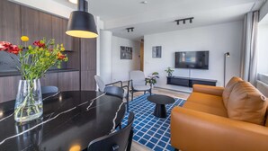 A modern living room with a black dining table, a sofa, a TV, and a large window. - Deluxe two bedroom apartment (Reykjavík)