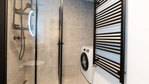 A modern bathroom with a glass-enclosed shower, a built-in washing machine, and a black metal towel rack. - Deluxe three bedroom apartment (Reykjavík)