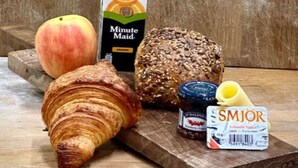 A wooden table with a croissant, a peach, a loaf of bread, a jar of jam, a carton of juice, and a bottle of cream. - Deluxe three bedroom apartment (Reykjavík)