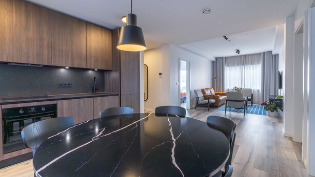 A modern kitchen with a black marble table, wooden cabinets, and a pendant light. - Deluxe three bedroom apartment (Reykjavík)