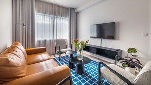 Una sala de estar moderna con un sofá, dos sillones, una mesa de centro, un televisor y una planta.