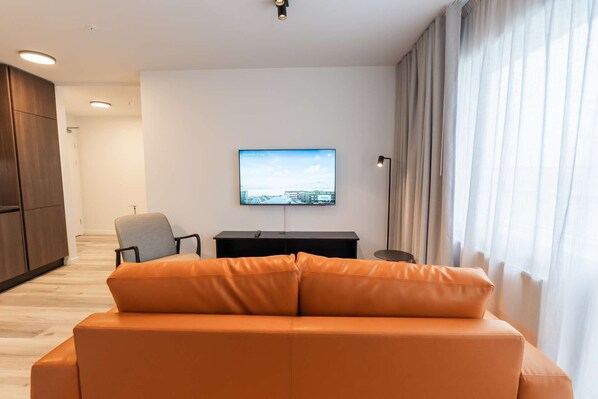Una sala de estar moderna con un sofá de cuero, un televisor de pantalla plana montado en la pared, un escritorio y una silla.