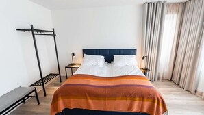 Una habitación de hotel moderna con una cama, un banco, una mesita de noche y una ventana con cortinas.