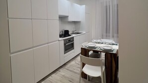 A modern kitchen with white cabinetry, a dining area with a wooden table and chairs, and a skylight above. - ARTPA Rome Apartments Trastevere Mameli (Roma)