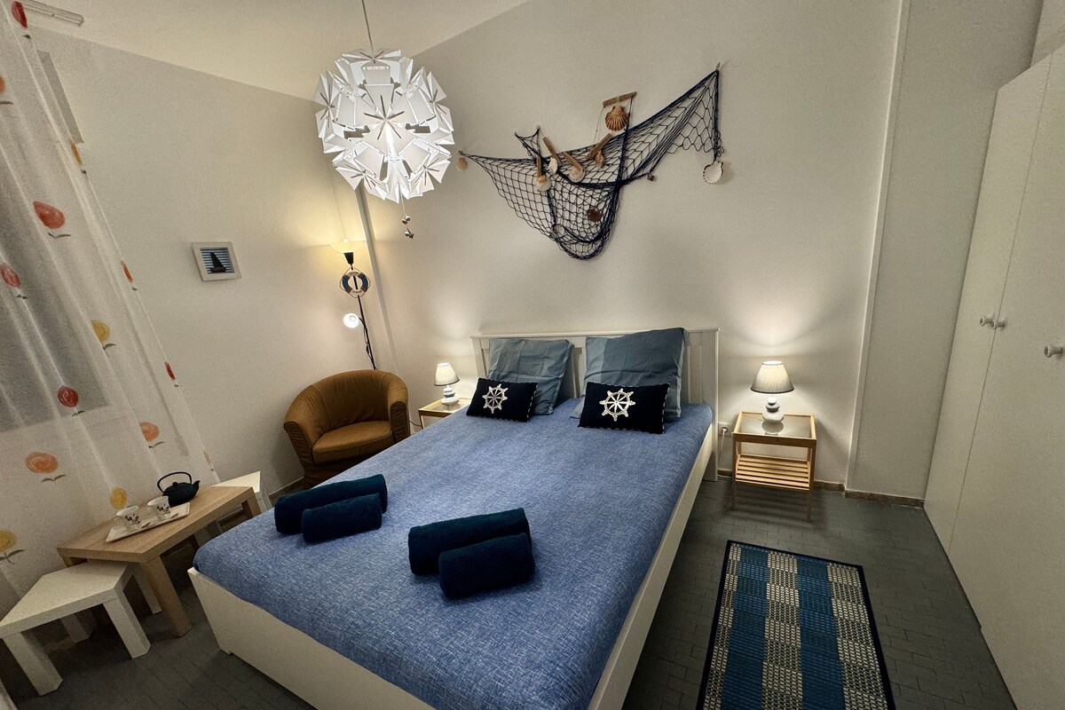 Ein Schlafzimmer mit einem großen Bett, einem Sessel, einem Nachttisch, einer Lampe, einer Dekoration und einem gemusterten Teppich.