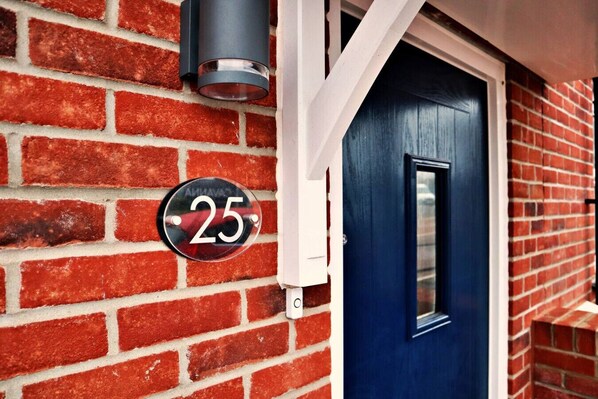 A red brick house with a blue door and a number plate displaying '25'.