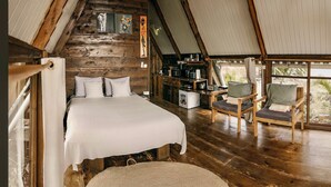 A cozy bedroom with a bed, a wooden chair, and a kitchenette in a rustic cabin. - Cozy A-frame Retreat in Zanzibar Nungwi Leo Glamping (Nungwi)