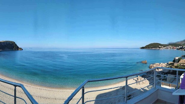 A coastal view with a beach, clear blue water, and a hillside with buildings. - Magic Ionian Apartments & Rooms (Himarë)