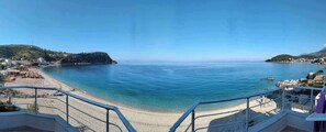 A coastal view with a beach, clear blue water, and a hillside with buildings. - Magic Ionian Apartments & Rooms (Himarë)