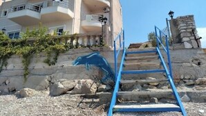 A multi-story building with balconies, a stone staircase, and a stone wall with a blue graffiti. - Magic Ionian Apartments & Rooms (Himarë)
