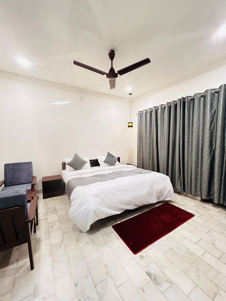 A bedroom with a bed, a chair, a nightstand, a ceiling fan, and a red rug.