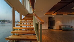 Un escalier en bois, doté d’une rampe verte, mène à une pièce avec une grande fenêtre donnant sur une étendue d’eau.