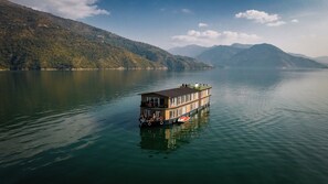 A houseboat with a balcony, situated on a calm lake surrounded by mountains. - Divine Lake Cruise (Tehri)